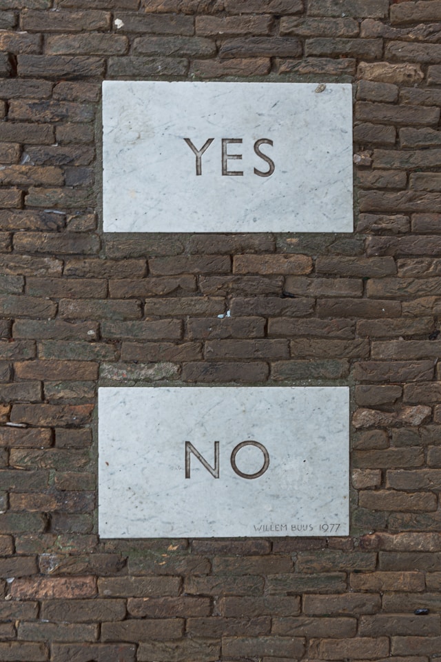 Two grey tiles read the phrases ‘Yes’ and ‘No’ respectively against a brick wall. 