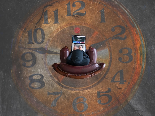 A shot from above of a person sitting in an armchair using a laptop. The chair is in the middle of a large clock.
