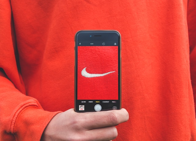 A person holds a phone up to their red sweater and takes a picture of the Nike logo.
