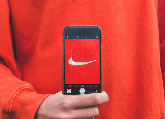 A person holds a phone up to their red sweater and takes a picture of the Nike logo.