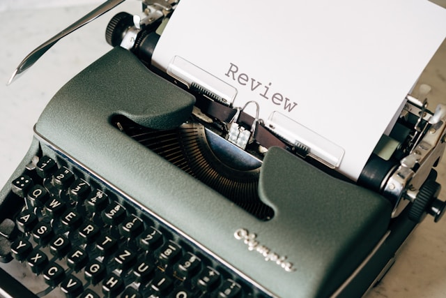 A close-up of a black and white typewriter with a piece of paper titled ‘Review’ in it.