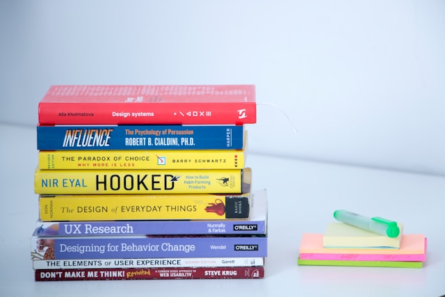A stack of books about UX on a white table.

