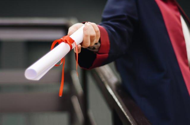 A person holds a white scroll with a red bow around it, representing a certificate. 