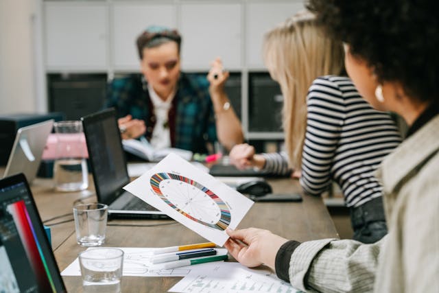 Three co-workers collaborate during a meeting. One co-worker holds a color wheel near their laptop.