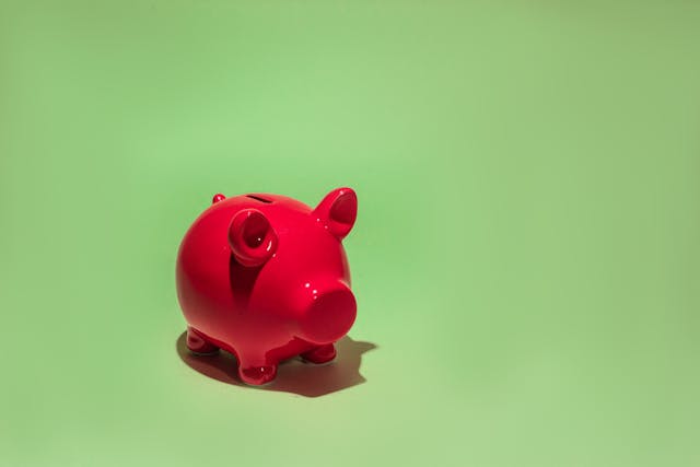 A close-up of a bright red piggy bank against a light green background. 

