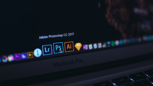 A close-up of a MacBook Pro screen. The cursor hovers over the Adobe Photoshop application.