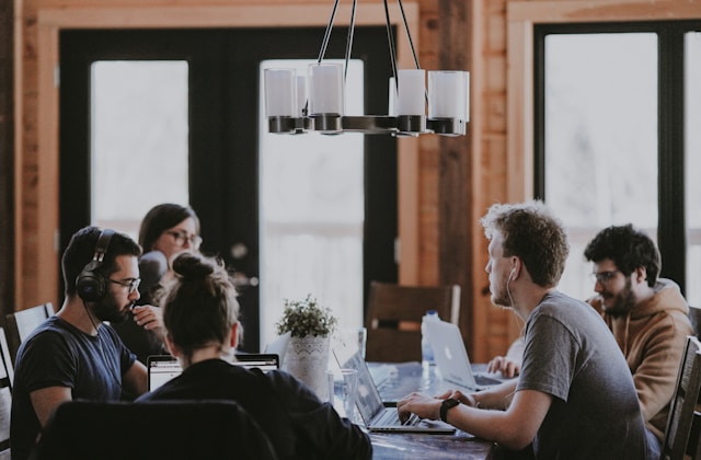 Five people sitting around a table as they work on their laptops. 