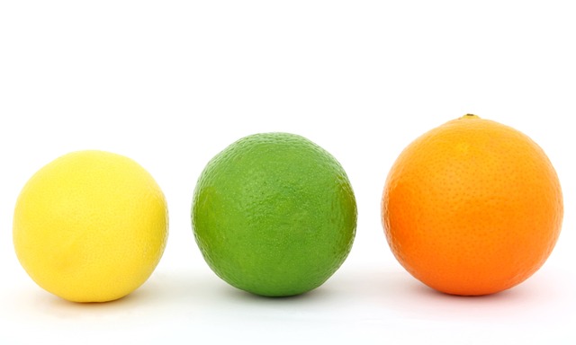 A lemon, lime, and orange sit next to each other, showcasing different sizes and proportions.