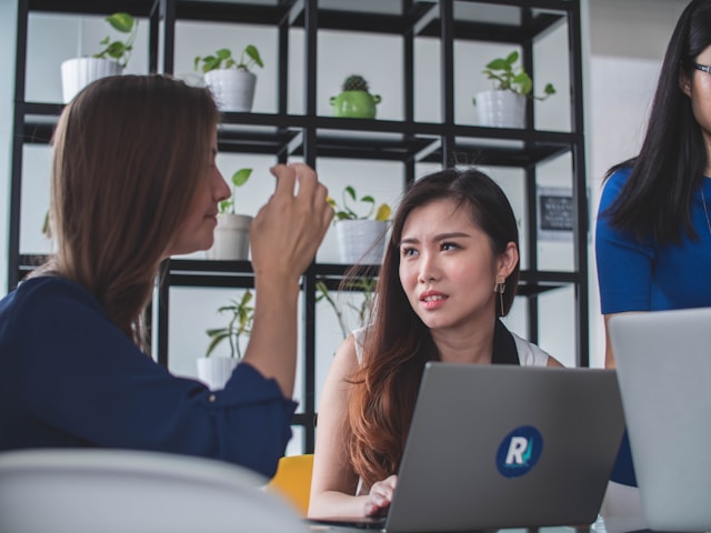 Two co-workers deliberate in front of a branded laptop. 