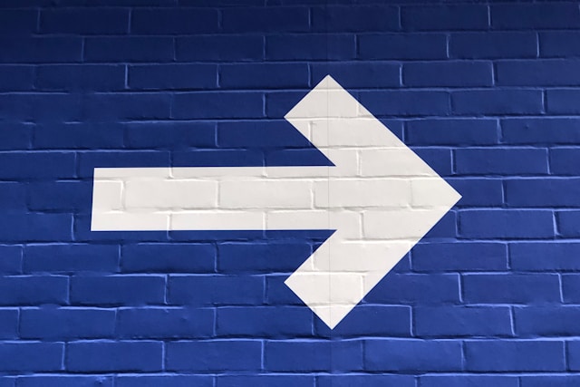 A white arrow painted on a blue brick wall representing directional flow. 
