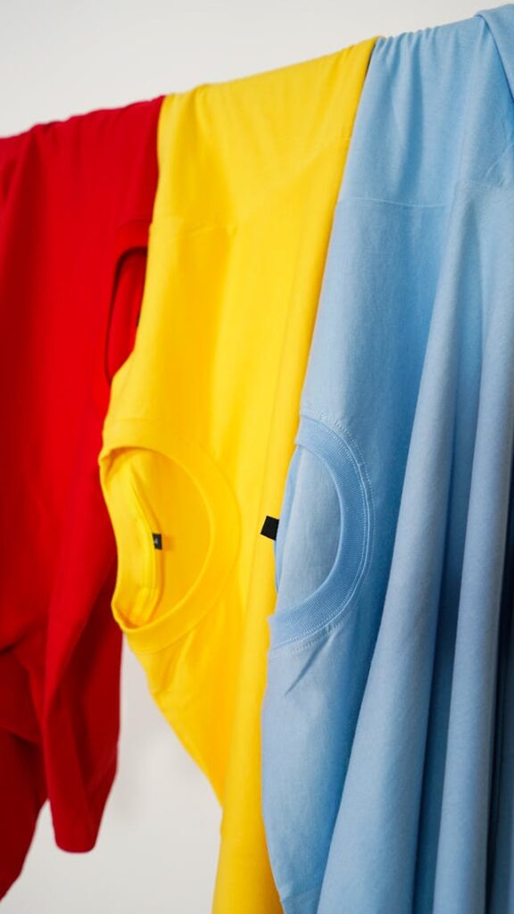 An image of three shirts drying on a clothing line. The shirts are red, yellow, and blue, respectively. 
