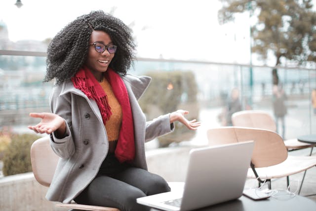 A woman sits at a table in front of her laptop, filming a video. 
