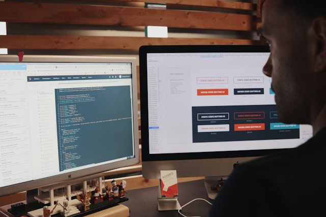 A person coding on one monitor with UI design options on another.