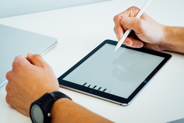 A person drawing on an iPad using a white stylus.