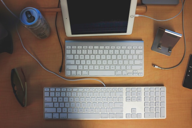 Two Apple keyboards and an iPad on a wooden desk.
