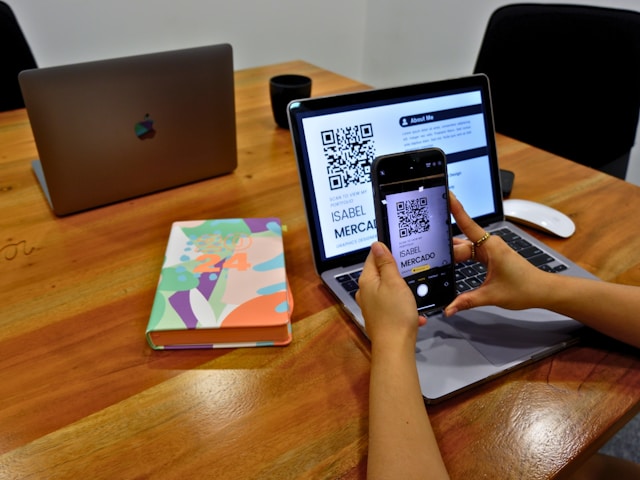 A person sitting at a table scanning a QR code on a resume with their phone.

