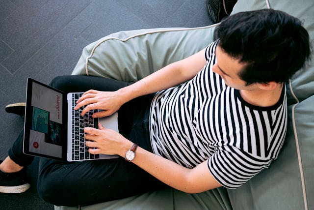 Overhead angle photo of a man using a laptop while sitting op a beanbag. 
