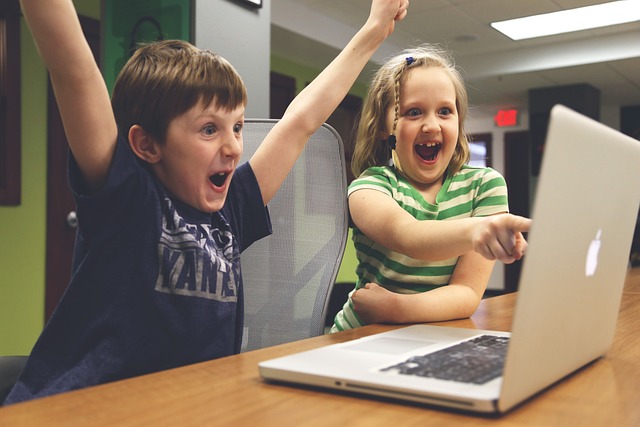 Two happy, excited children sitting in front of a silver laptop. 
