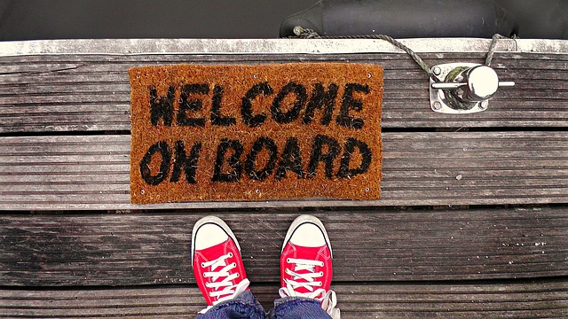 A bird's-eye view of a person wearing red shoes standing over a brown mat that reads “Welcome On Board.”