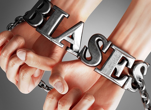 An illustration of human hands bound together with silver handcuffs that spell the word “Biases.”