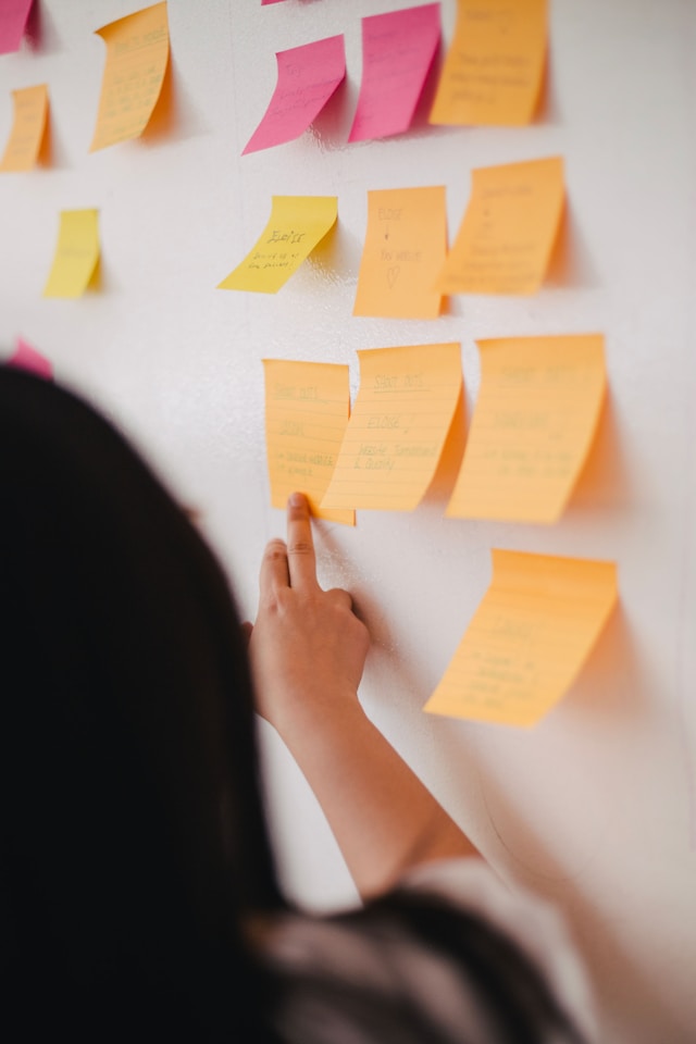 A UX researcher looks at a whiteboard that displays a series of notes on colorful sticky notes.  
