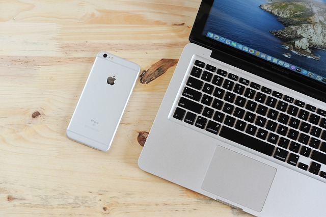 A birds-eye view of a silver iPhone next to a silver MacBook. 
