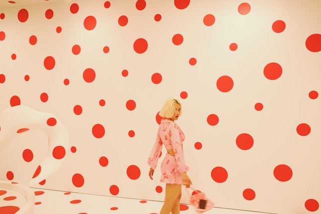An image of a woman standing in front of a large background that consists of red polka dots. 
