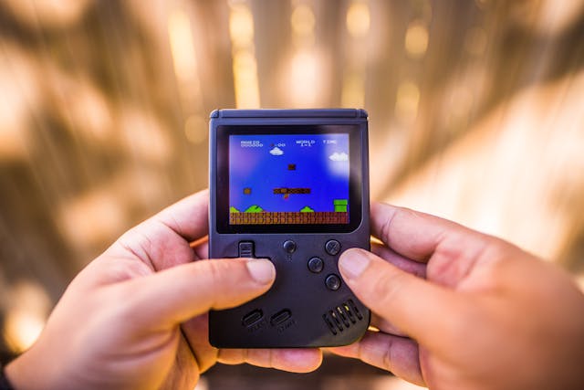 A close-up of someone playing a Super Mario game on a dark blue Game Boy console. 
