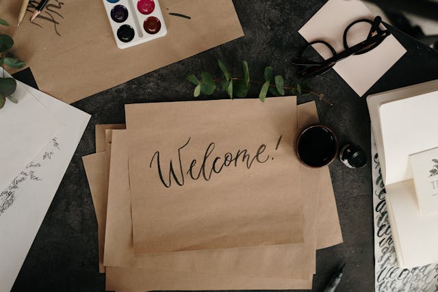 A bird’s-eye view of a brown piece of paper that reads the phrase “Welcome!” in a calligraphic font. 
