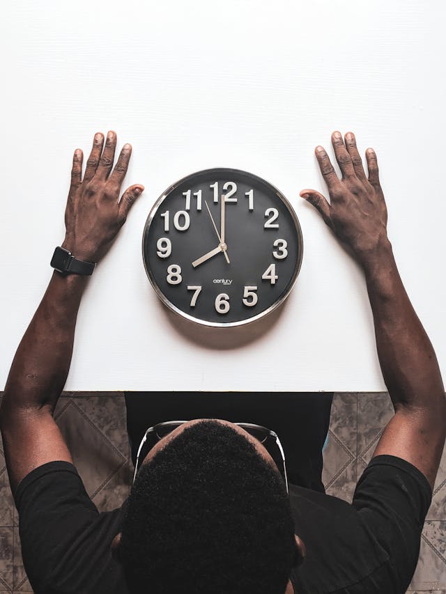 A bird’s-eye view of a man sitting at a white table in front of a black and white clock.