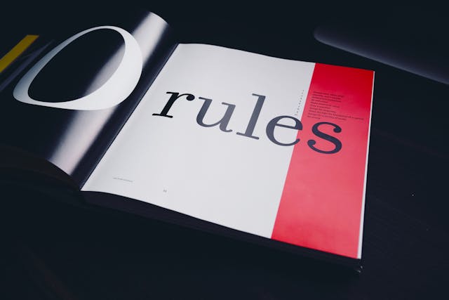 A close-up of an open book that reads the word “rules” in bold, black font. 
