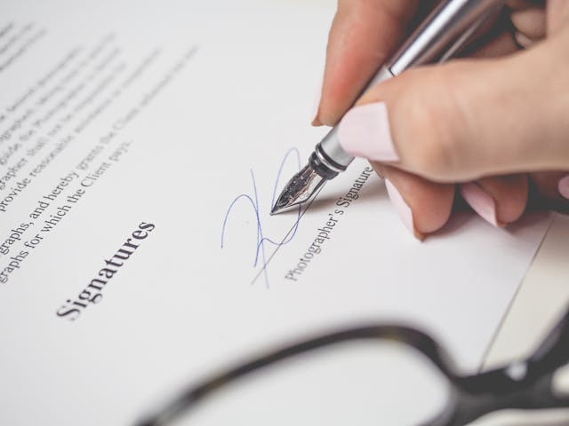 A close-up of someone signing a contract using a silver fountain pen.