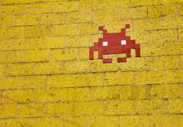 A red pixel-like alien from the arcade game Space Invaders on a yellow brick wall. 
