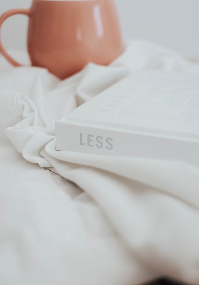 A close-up of a white book with the title “Less” on top of white fabric, representing simplicity. 
