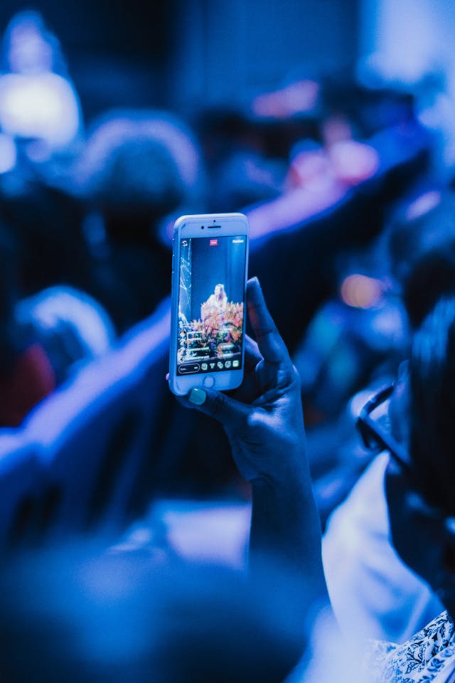 A person holding their phone to live stream a musical performance with one hand.