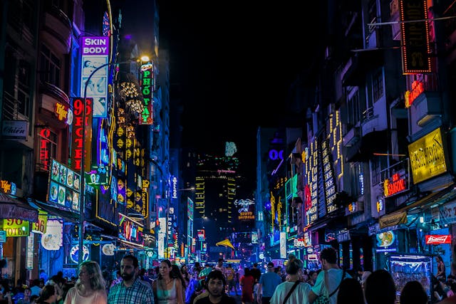 A crowd of people walk down a street that is full of differently colored neon signs.