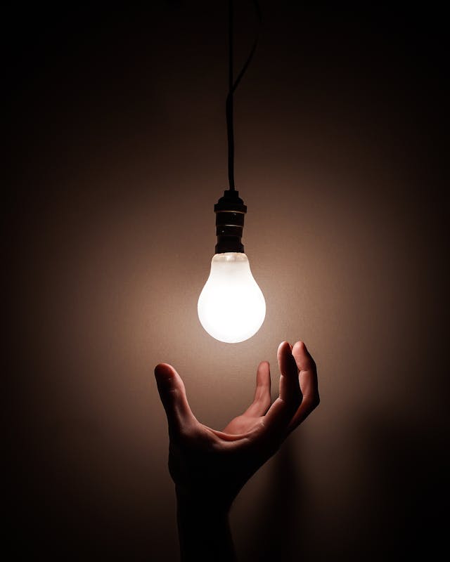 A person holding their hand out to a brightly lit bulb that represents inspiration. 
