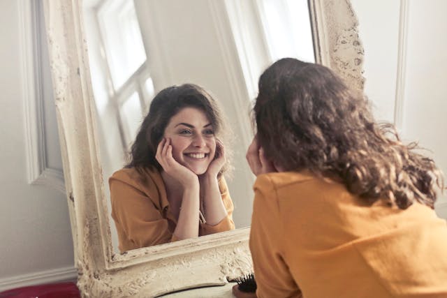 A woman smiling while looking at herself in the mirror. 
