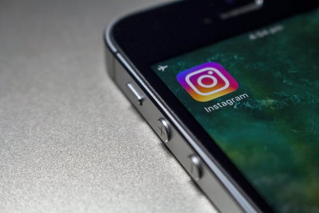 A close-up of a black mobile phone that displays the icon for Instagram’s app. 
