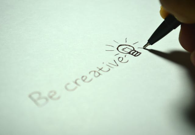 A close-up of someone writing the phrase “Be creative” with a drawing of a light bulb next to it.