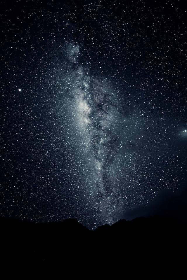 A silhouette of a mountain sits underneath a starry, grey night sky. 
