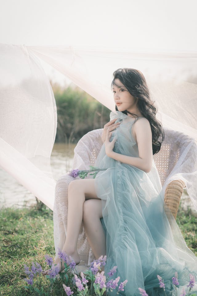 A girl sitting outside on a chair in the sun, wearing pale blue tulle fabric.