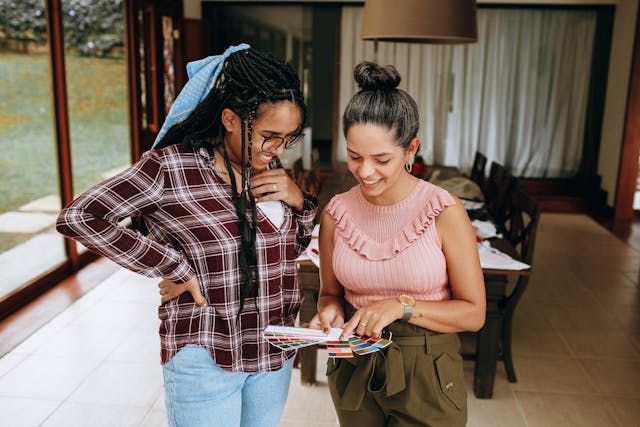 Two women smile while looking at a color swatch fan, symbolizing collaboration. 
