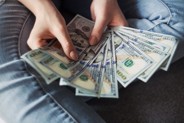 A close-up of a person holding a series of fanned-out US dollar banknotes. 