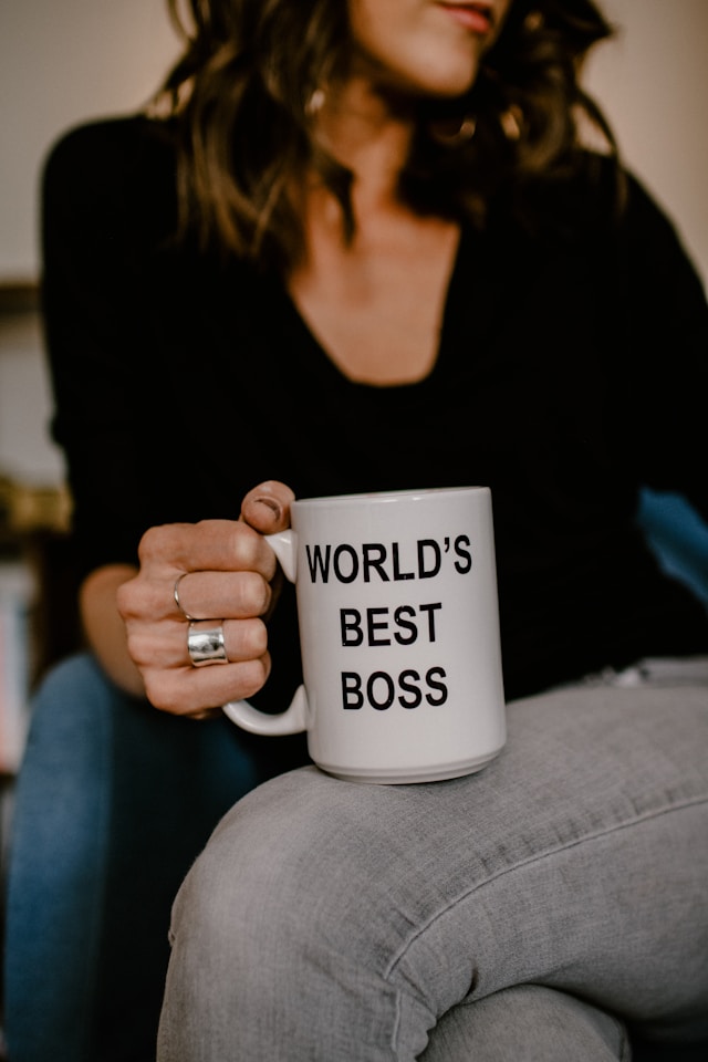 A close-up of a woman holding a white mug that reads the phrase “World’s Best Boss.”
