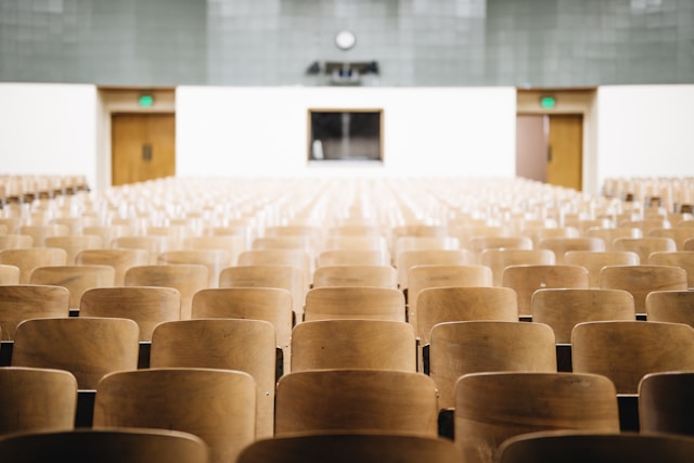 A large group of empty, brown chairs in a university lecture hall. 
