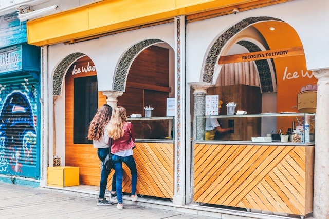 Two people purchasing ice cream from a small ice cream store.
