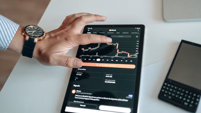A person tapping on a tablet with a fluctuating graph.