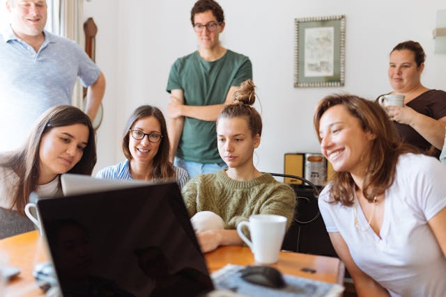 A group of people gathered around a table looking at a laptop.