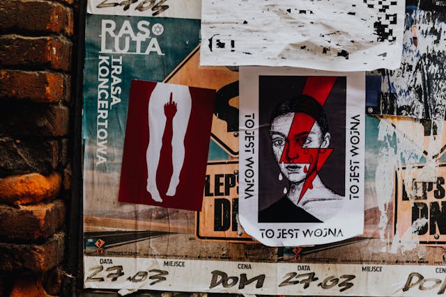 A series of punky, rebellious posters and leaflets are stuck to a brick wall. 
